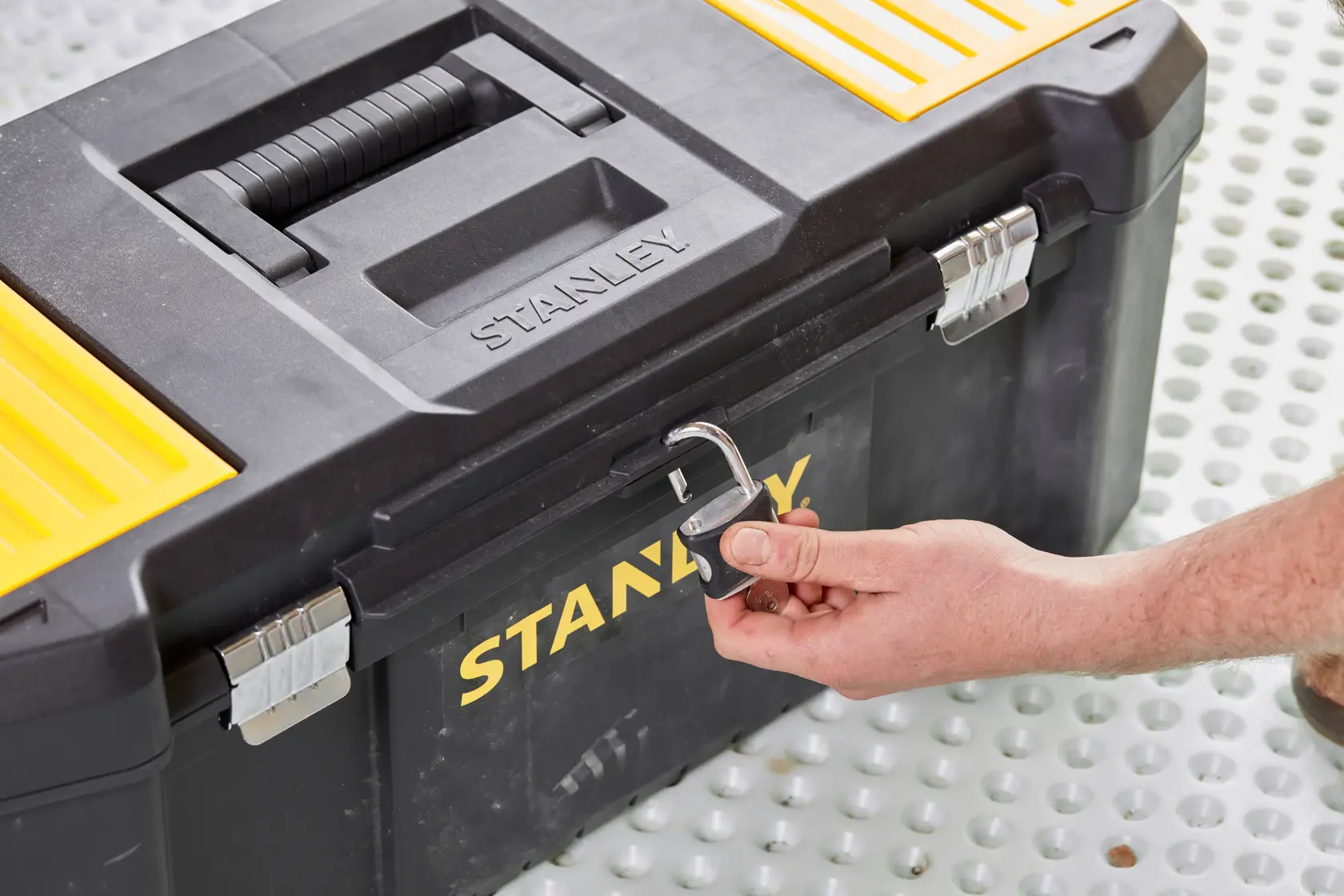 STANLEY STST82976-1 cassetta degli attrezzi angolo frontale, nera e gialla con lucchetto aperto da una mano.