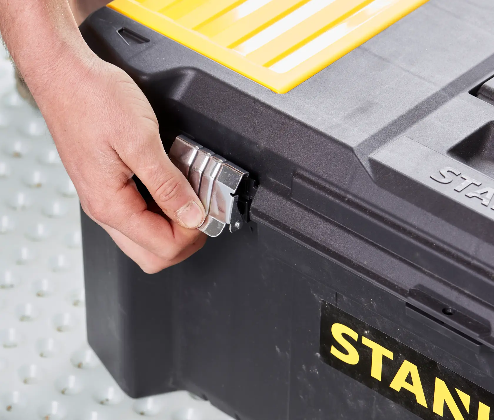 STANLEY STST82976-1 cassetta degli attrezzi in primo piano, mano sblocca la chiusura metallica, custodia in plastica nero e giallo.