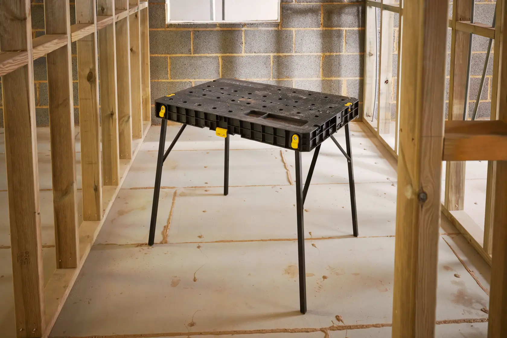 STANLEY STST83492-1 banco da lavoro, piano in plastica nera con gambe pieghevoli, mostrato in contesto di costruzione.