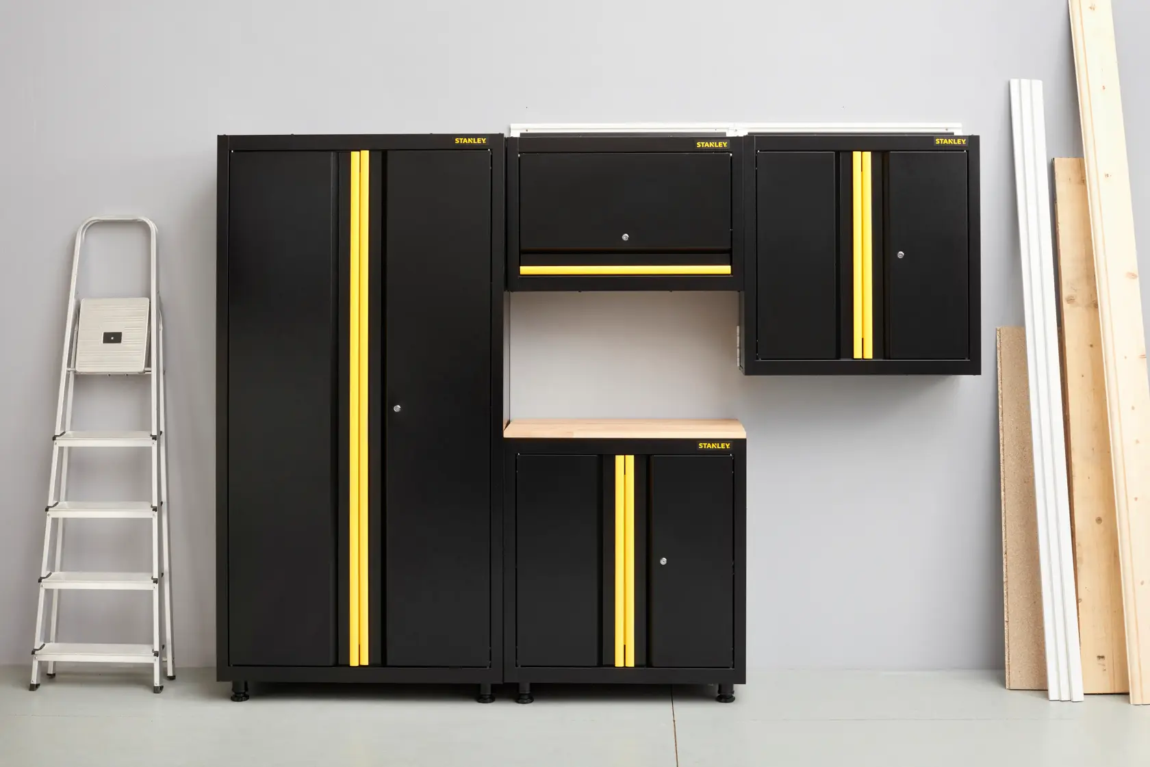 STANLEY STST97598-1 set di armadietti neri e gialli per garage, vista frontale, con scala e assi di legno.