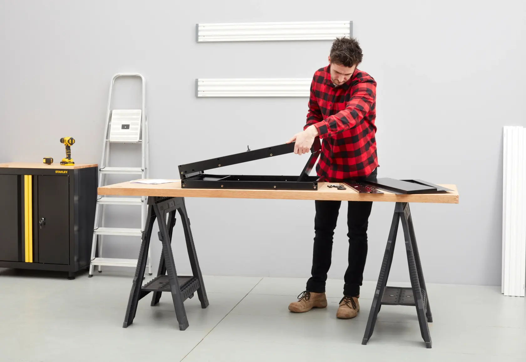 Foto del banco da lavoro STANLEY STST97599-1 in officina, persona che assembla telaio in metallo nero su piano in legno.