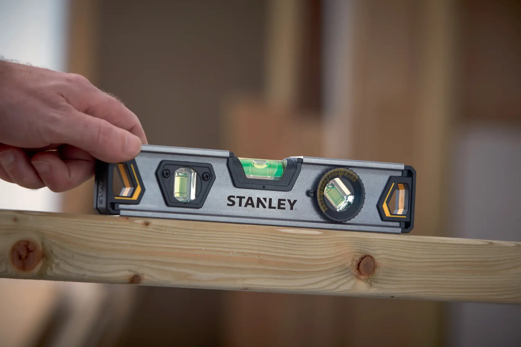 STANLEY XTHT0-42495 livella tenuta su trave di legno, ambiente di costruzione, angolo ravvicinato.